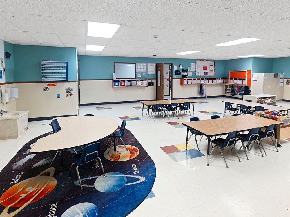 Empty classroom with small tables and chairs, and a planet-themed rug