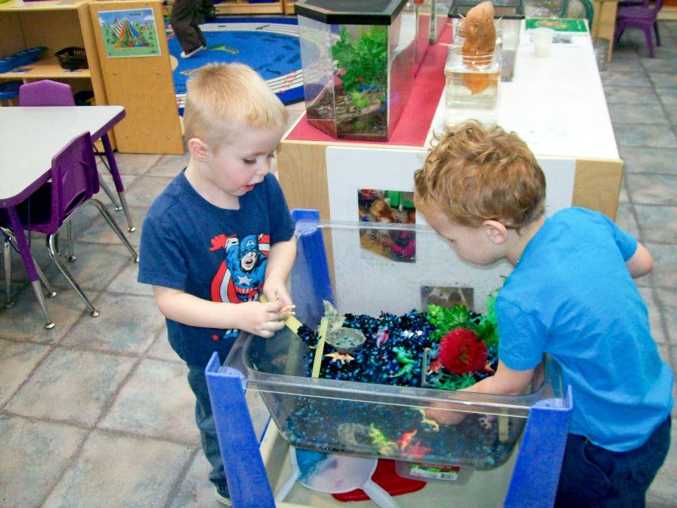Two children playing with toys in a water table