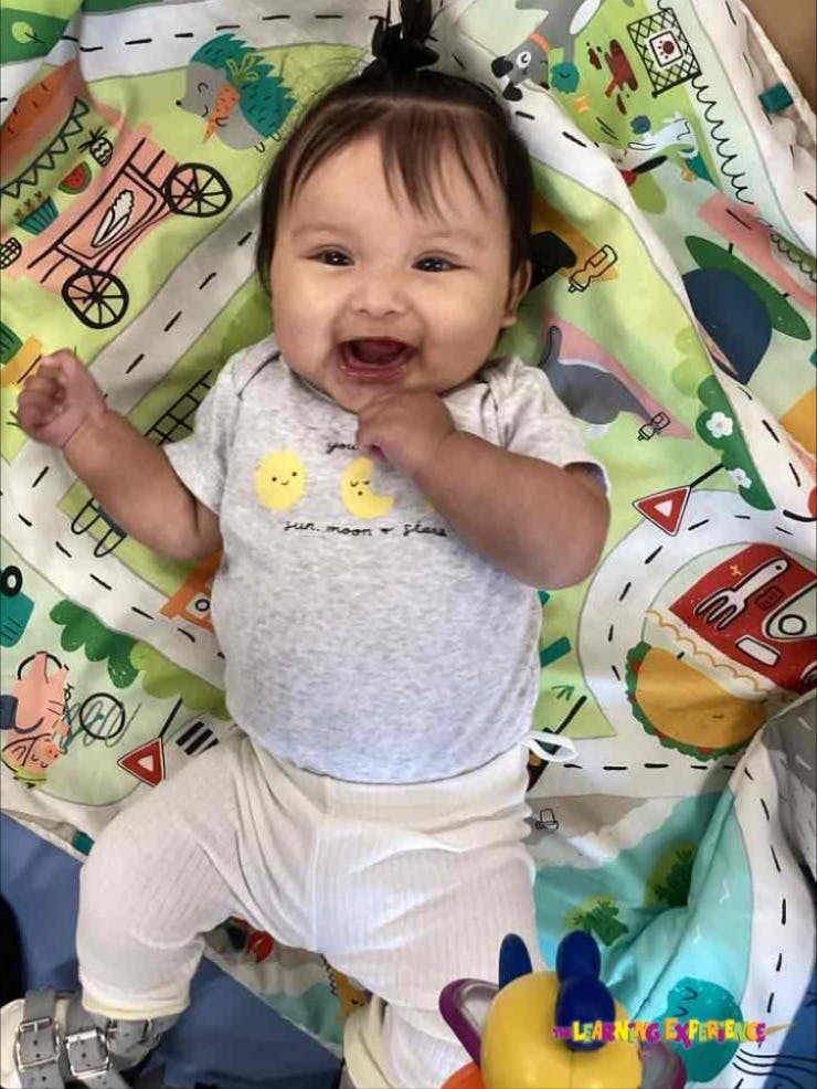 Child lying on a playmat, smiling with mouth open