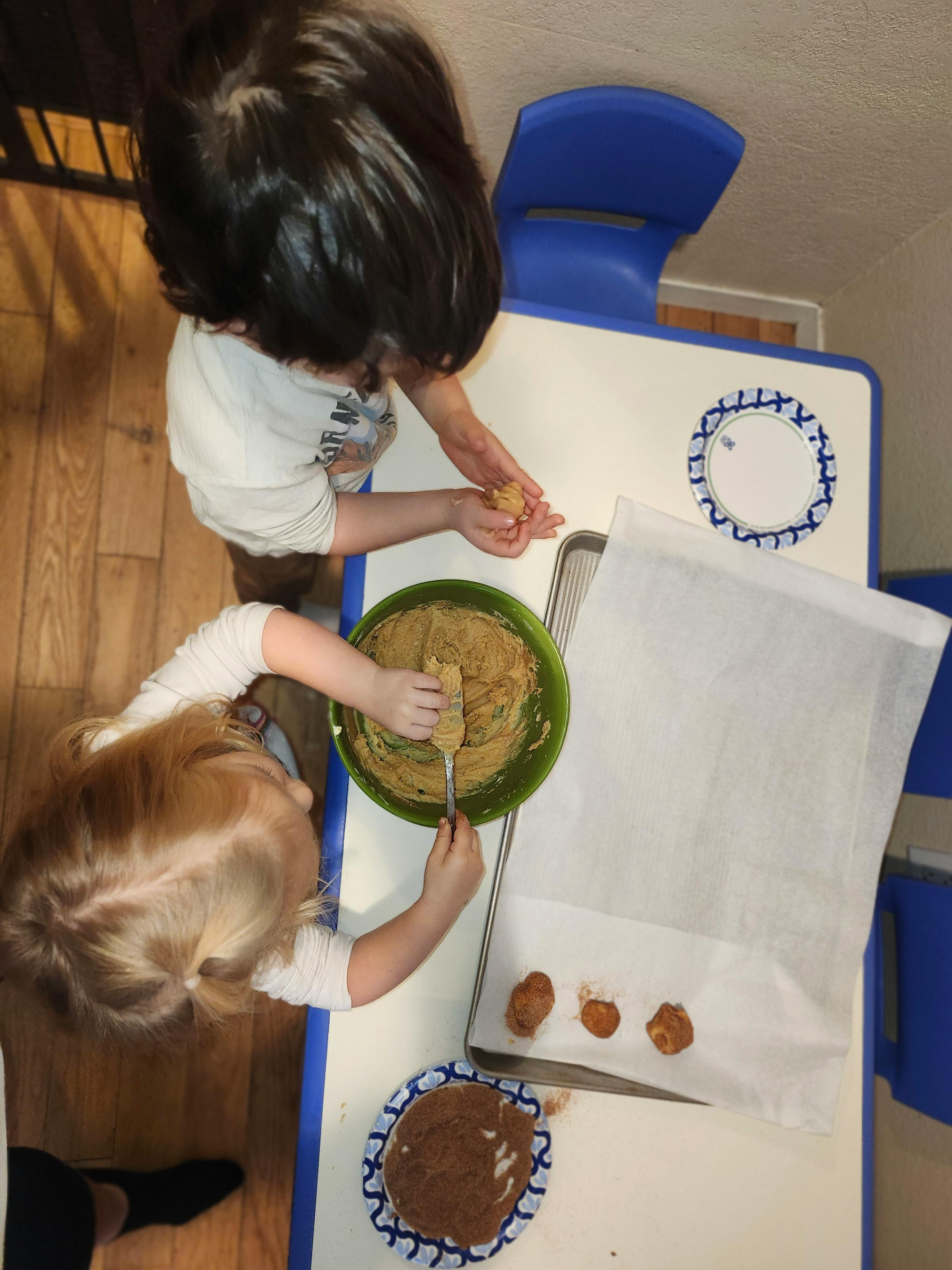 Two children making cookies, one holding dough, the other stirring a bowl