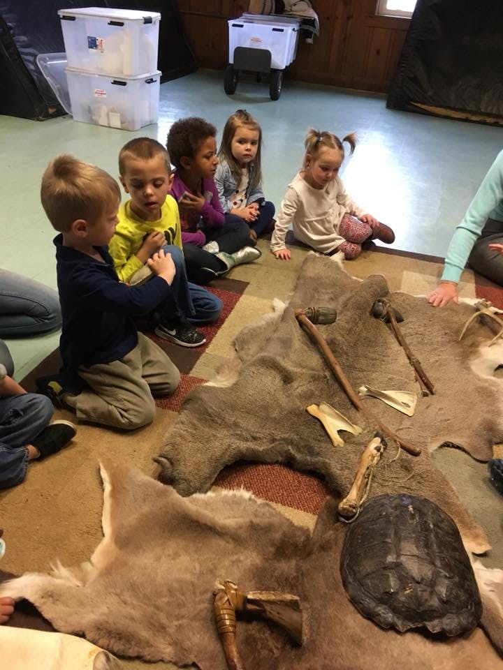 Children sitting on a rug looking at animal hides and tools