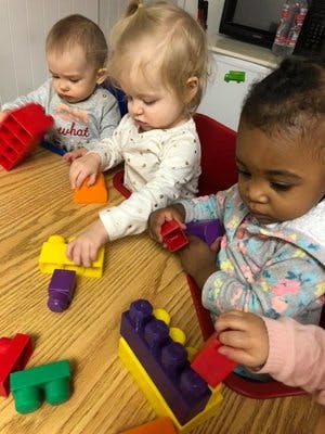 Three children playing with colorful building blocks at a table