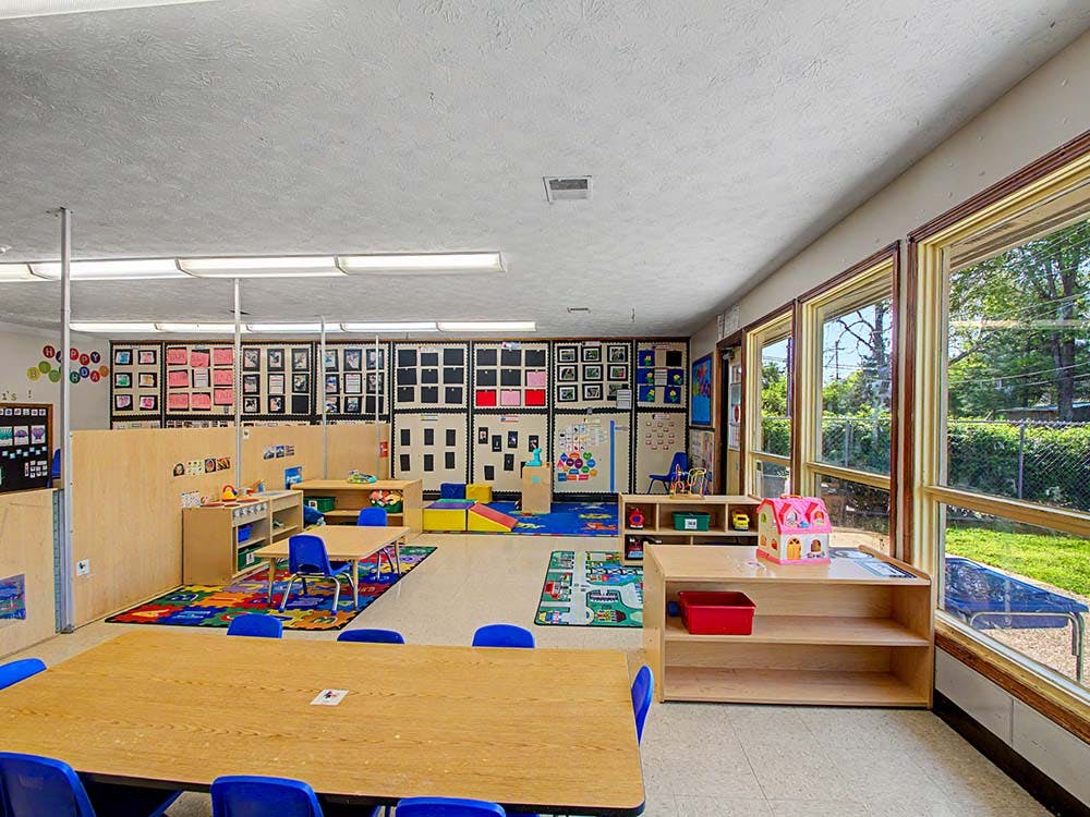 Empty classroom with small tables, chairs, and play areas