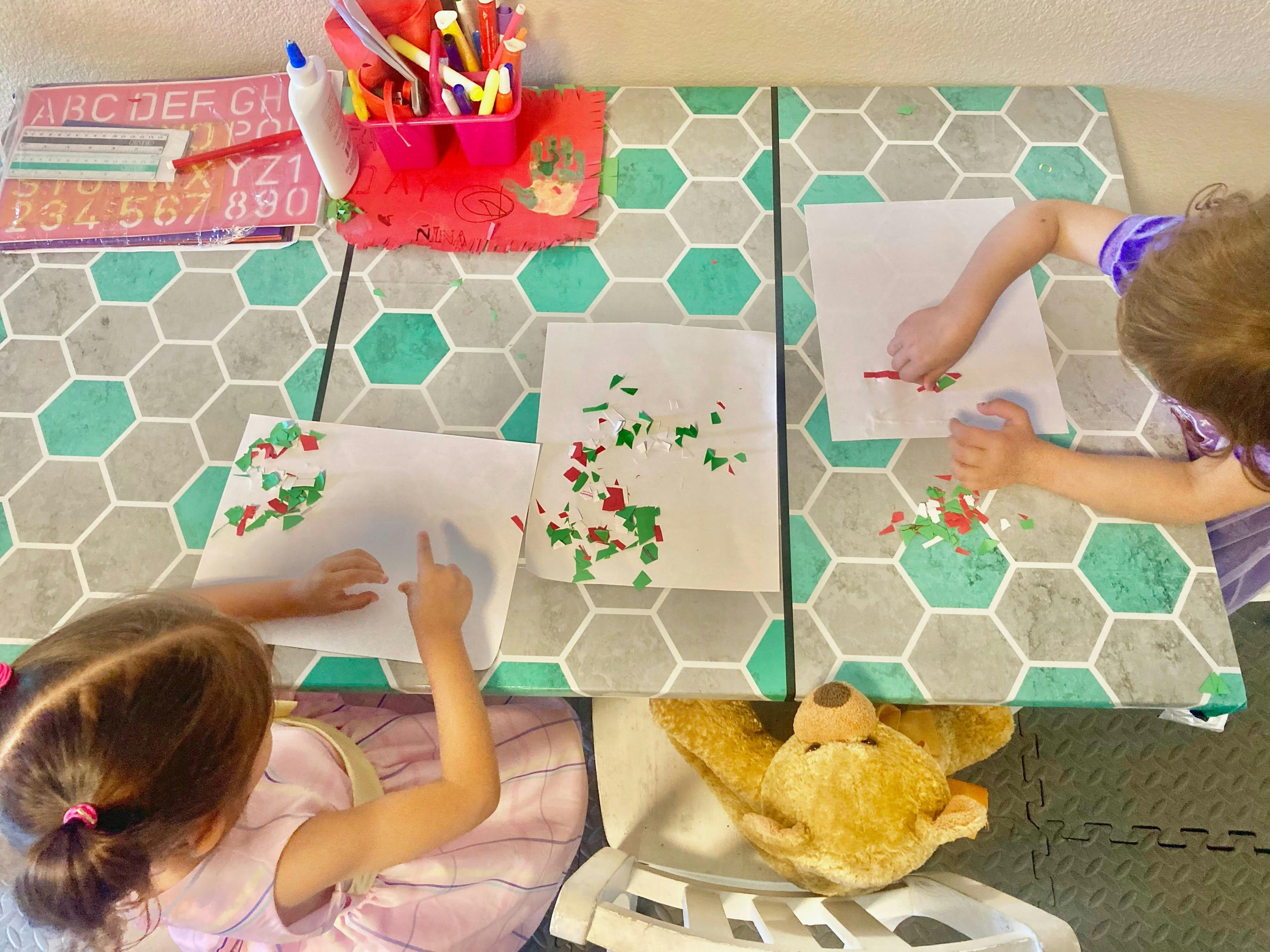 Two children doing crafts at a table with paper and colorful confetti