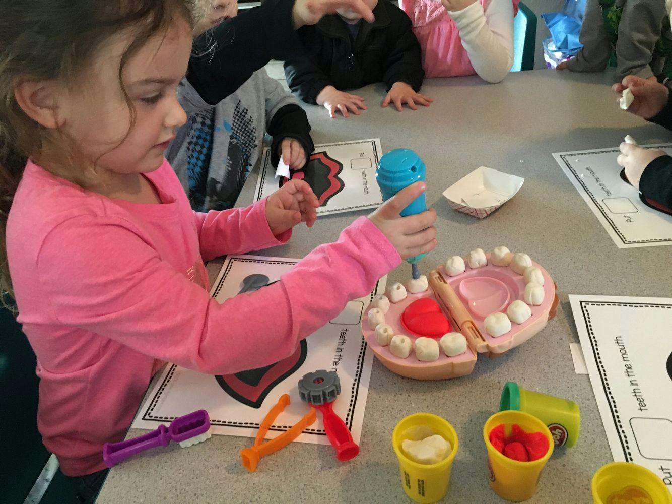 Child holding a blue toothbrush over a model of teeth