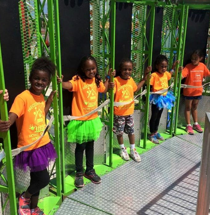 Five children standing on a platform holding onto green bars