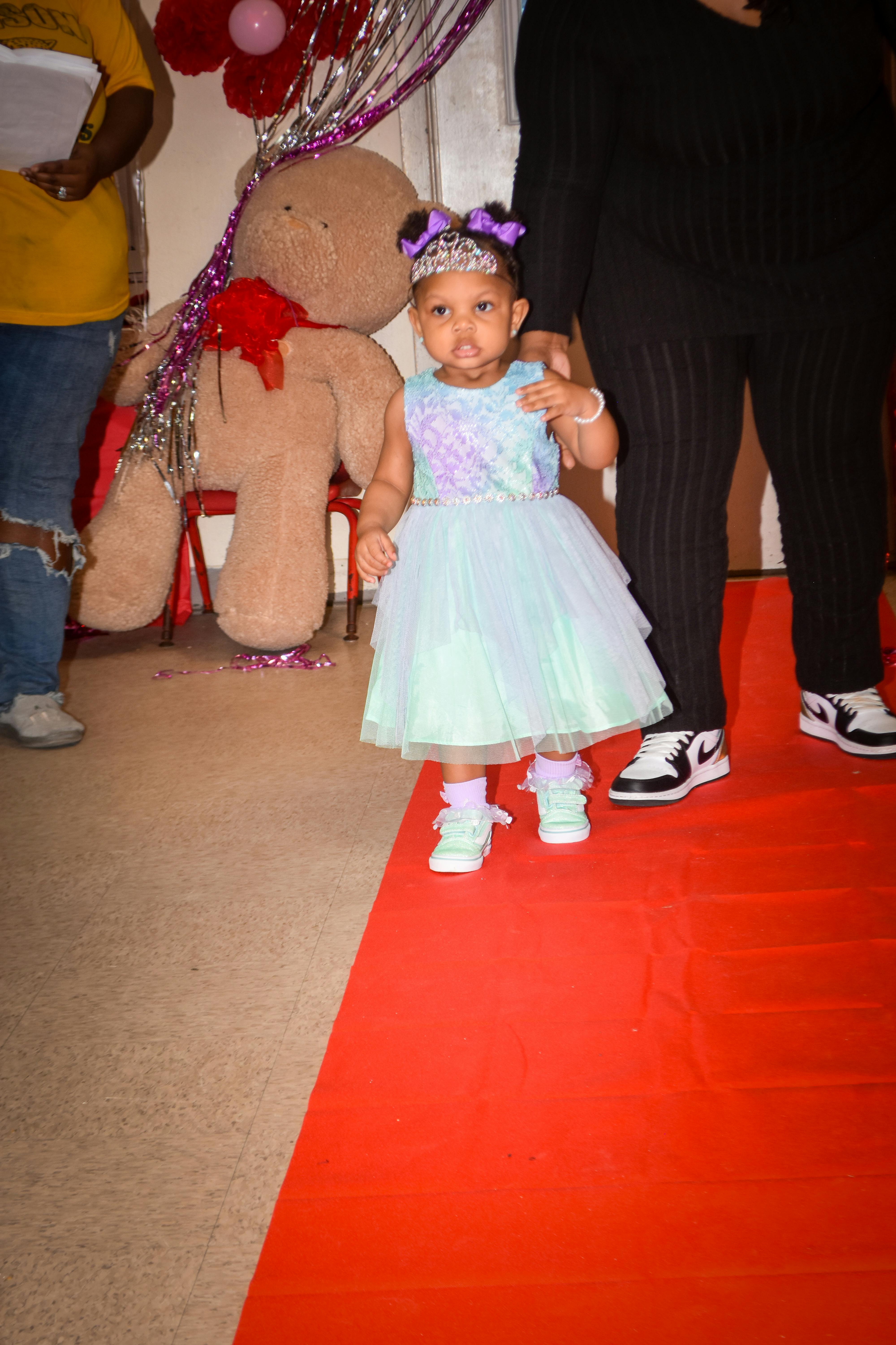Child in a light blue and purple dress with a tiara and purple bows