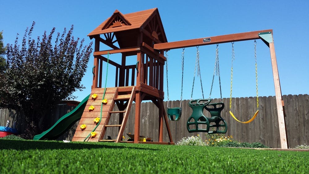 Wooden playground set with swings, slide, and climbing wall