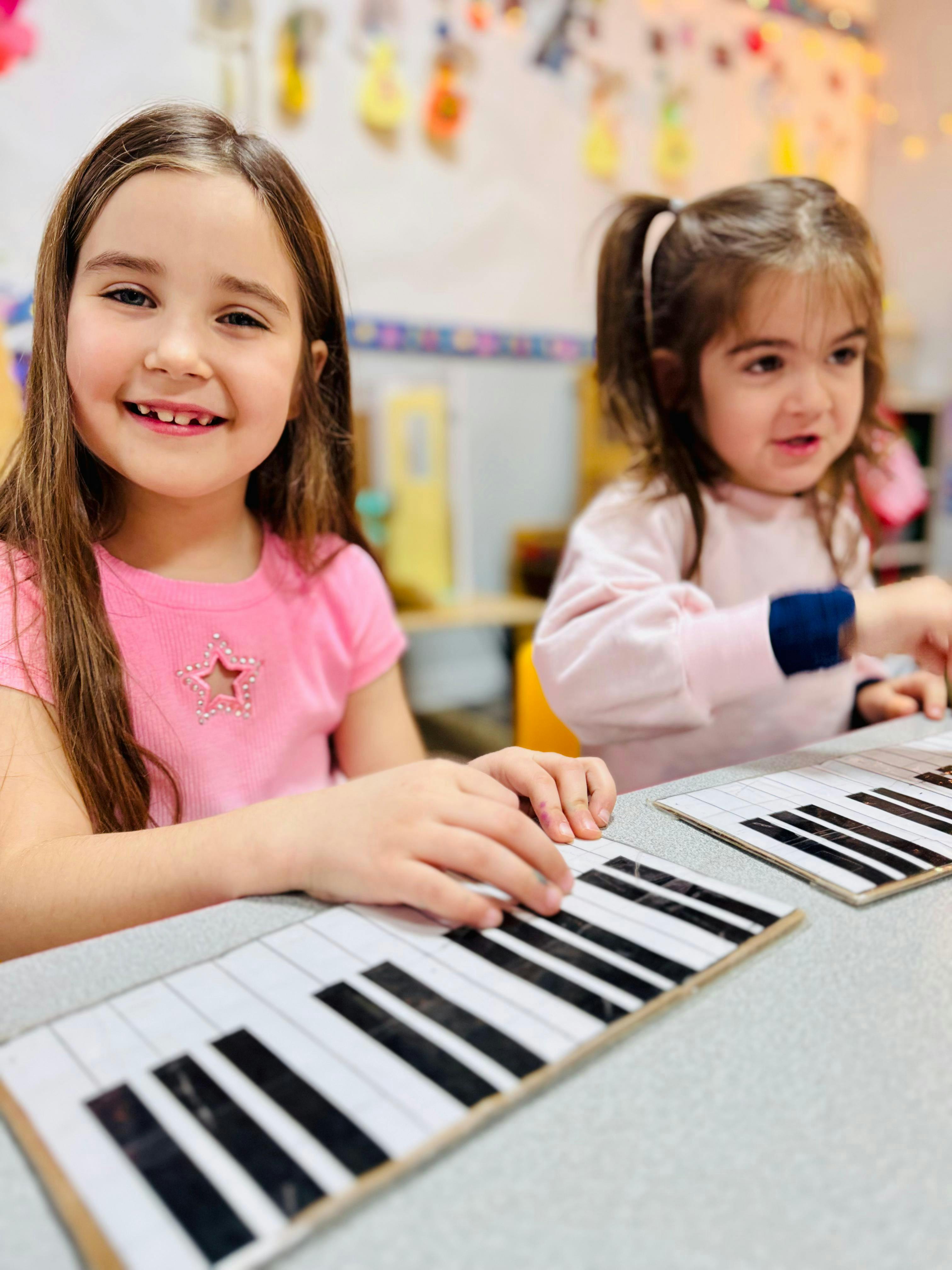 Two children practicing on paper piano keyboards in a classroom