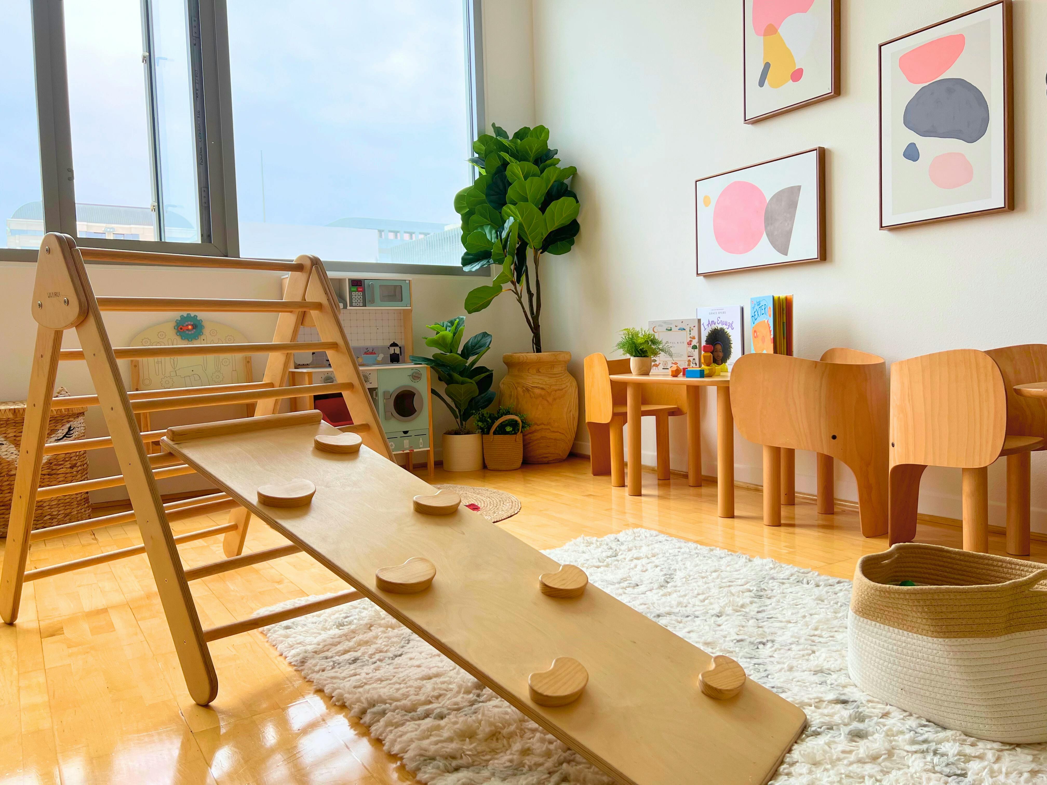 Indoor play area with a wooden climbing frame and slide, small tables and chairs