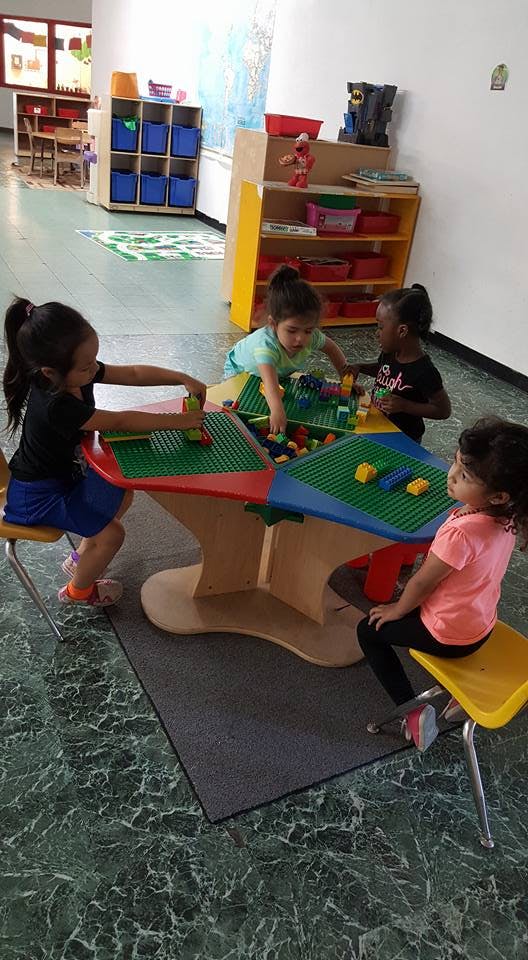 Four children playing with building blocks at a table in a classroom