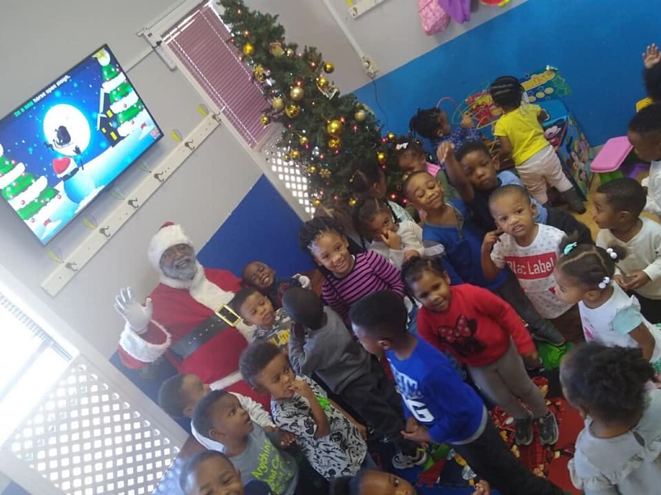 Children gathered around a person dressed as Santa Claus next to a Christmas tree