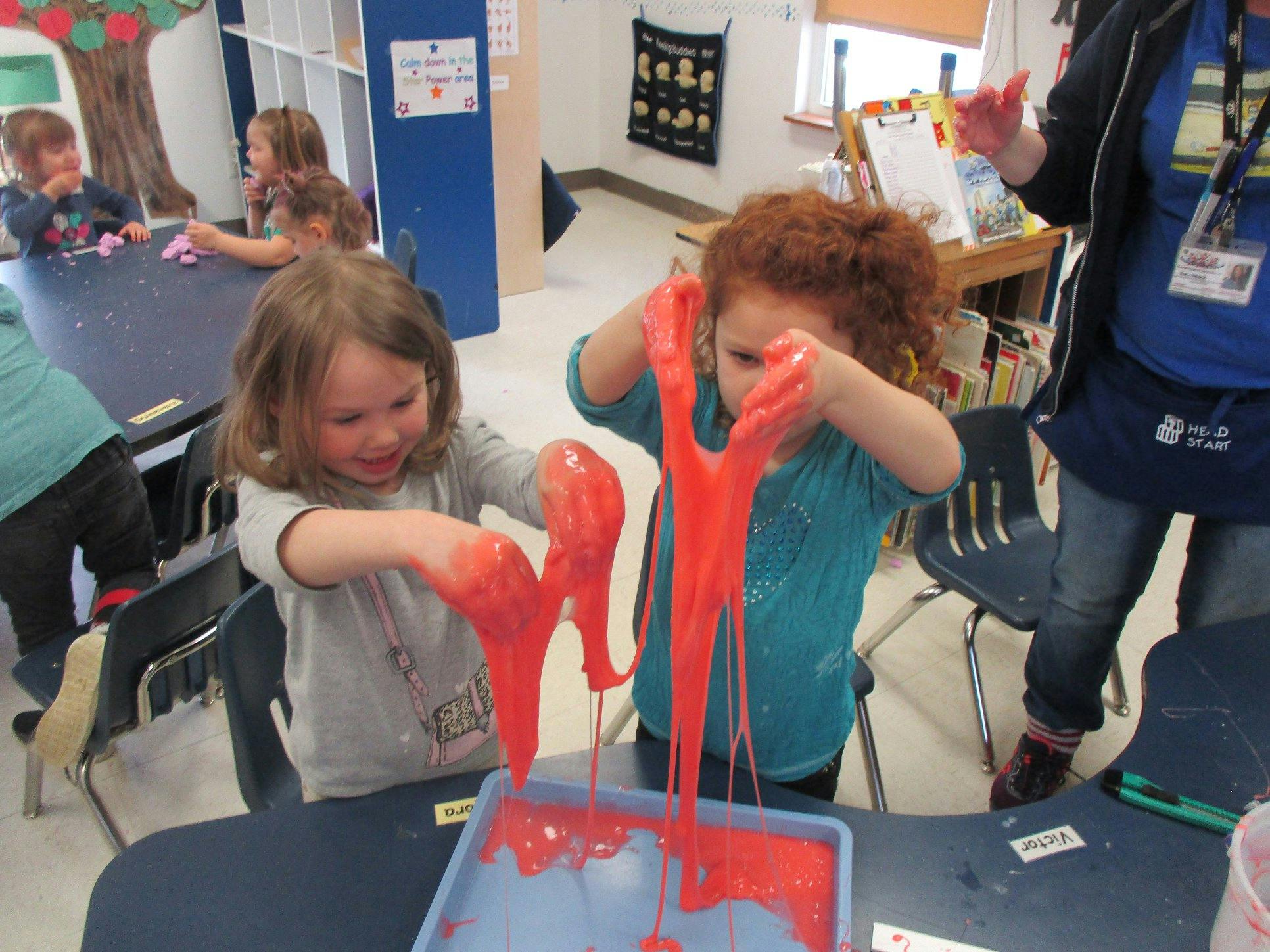 Two children playing with red slime in a classroom
