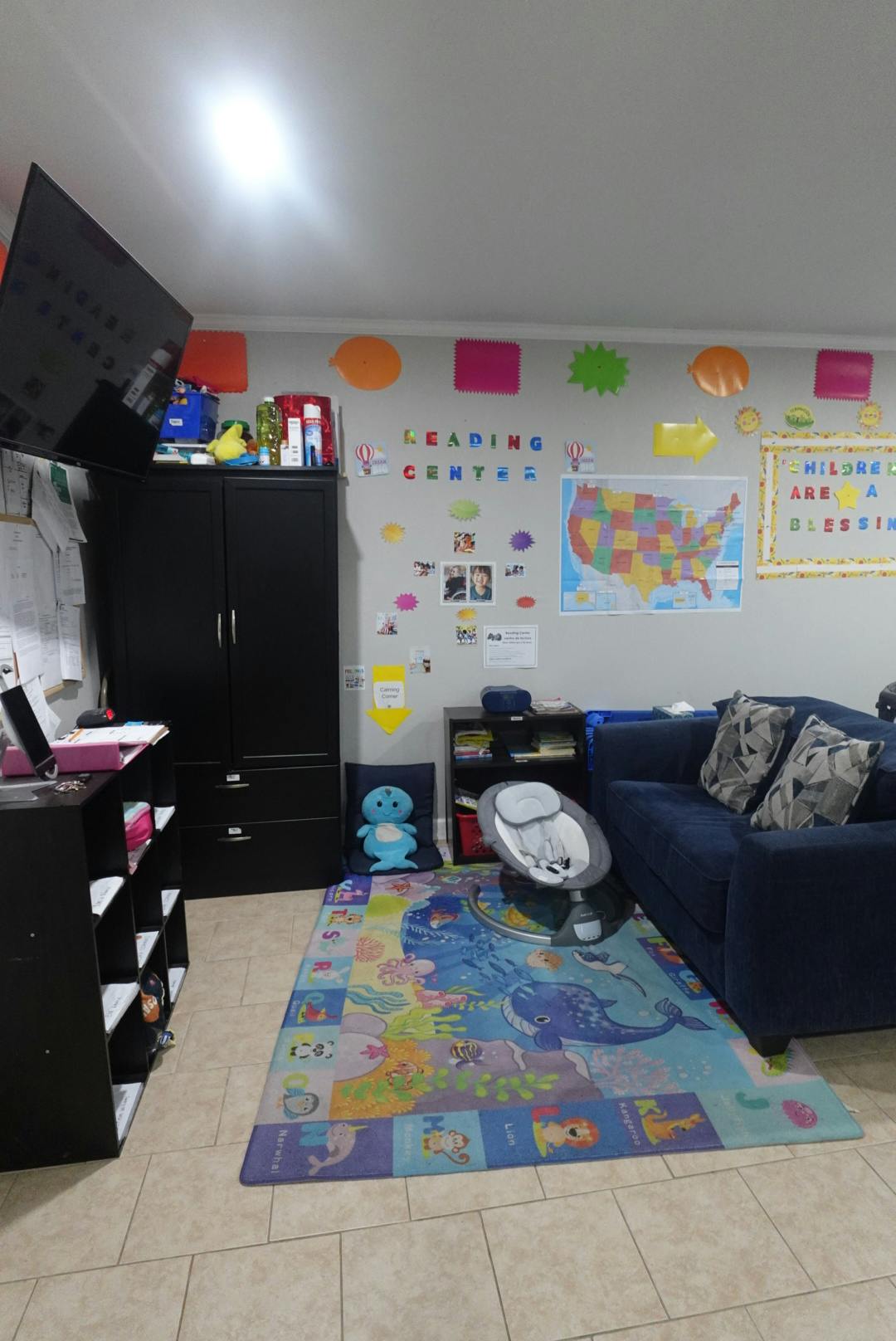 Room with a colorful playmat, blue sofa, and wall decorations including a map