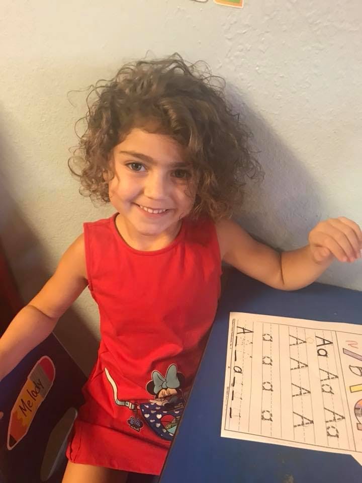 Child with curly hair sitting at a table with an alphabet worksheet