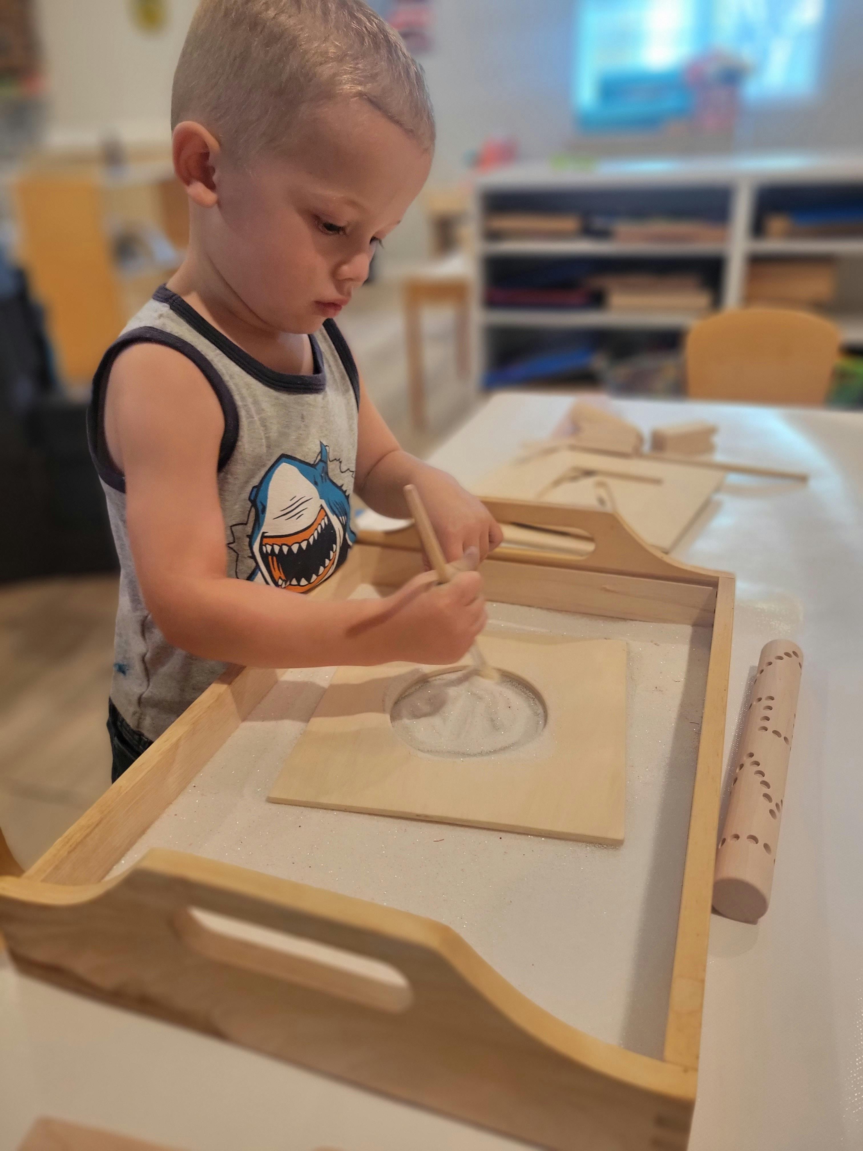 Child drawing in a sand tray with a stick