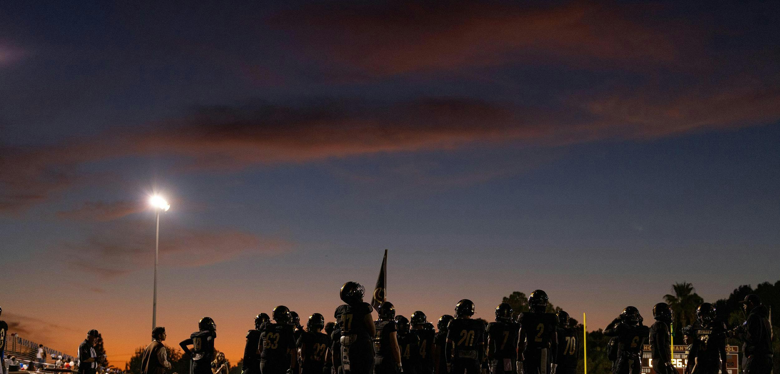 Football team standing under a bright stadium light at dusk