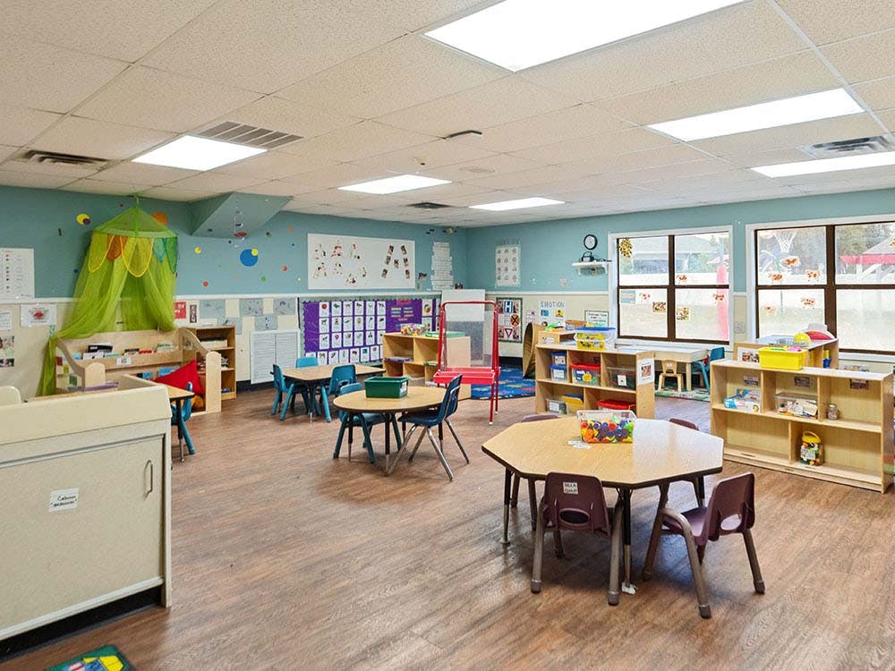Empty colorful preschool classroom with tables, chairs, and learning materials