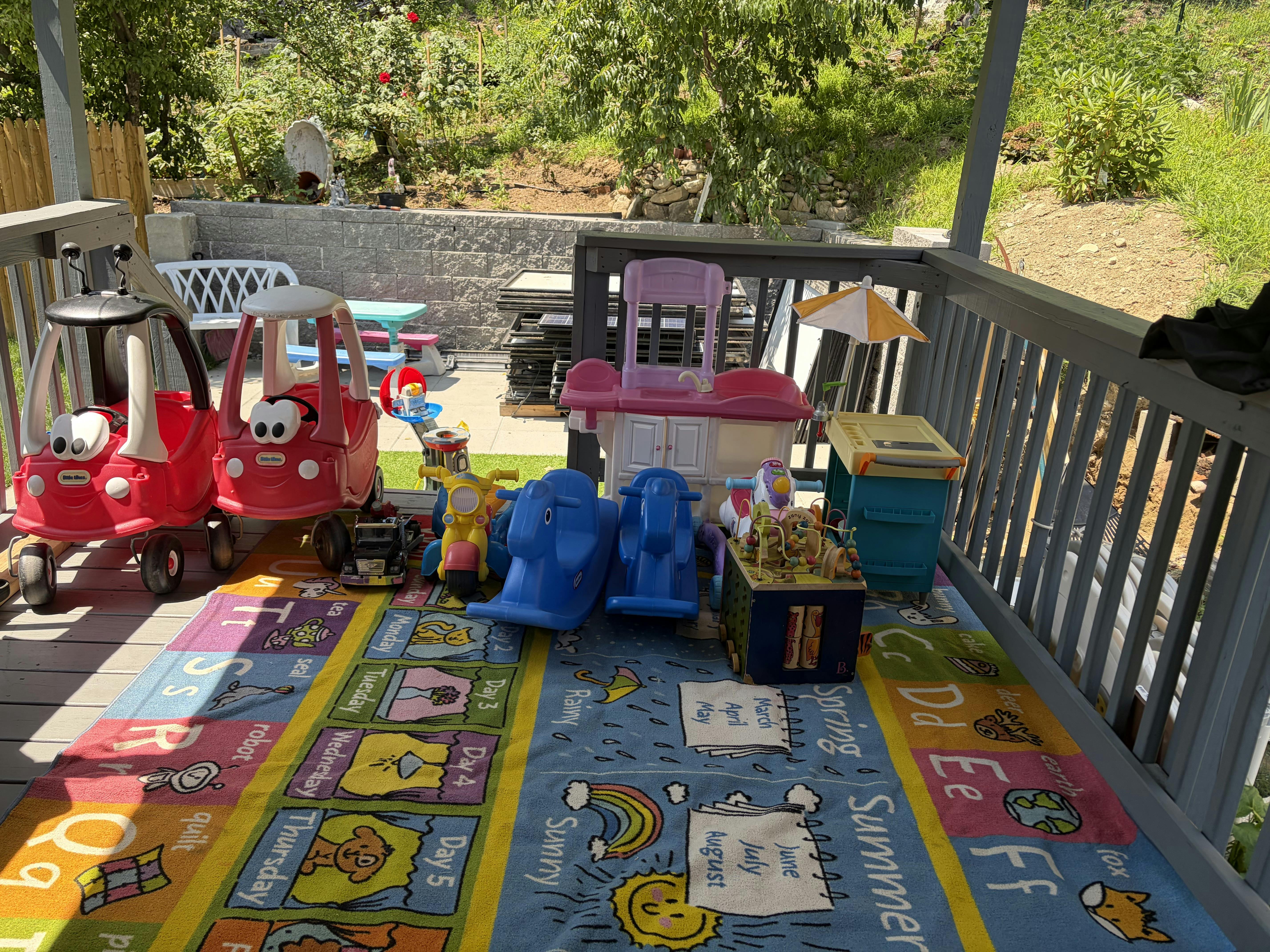 Collection of various plastic toys on a colorful alphabet play mat on a porch