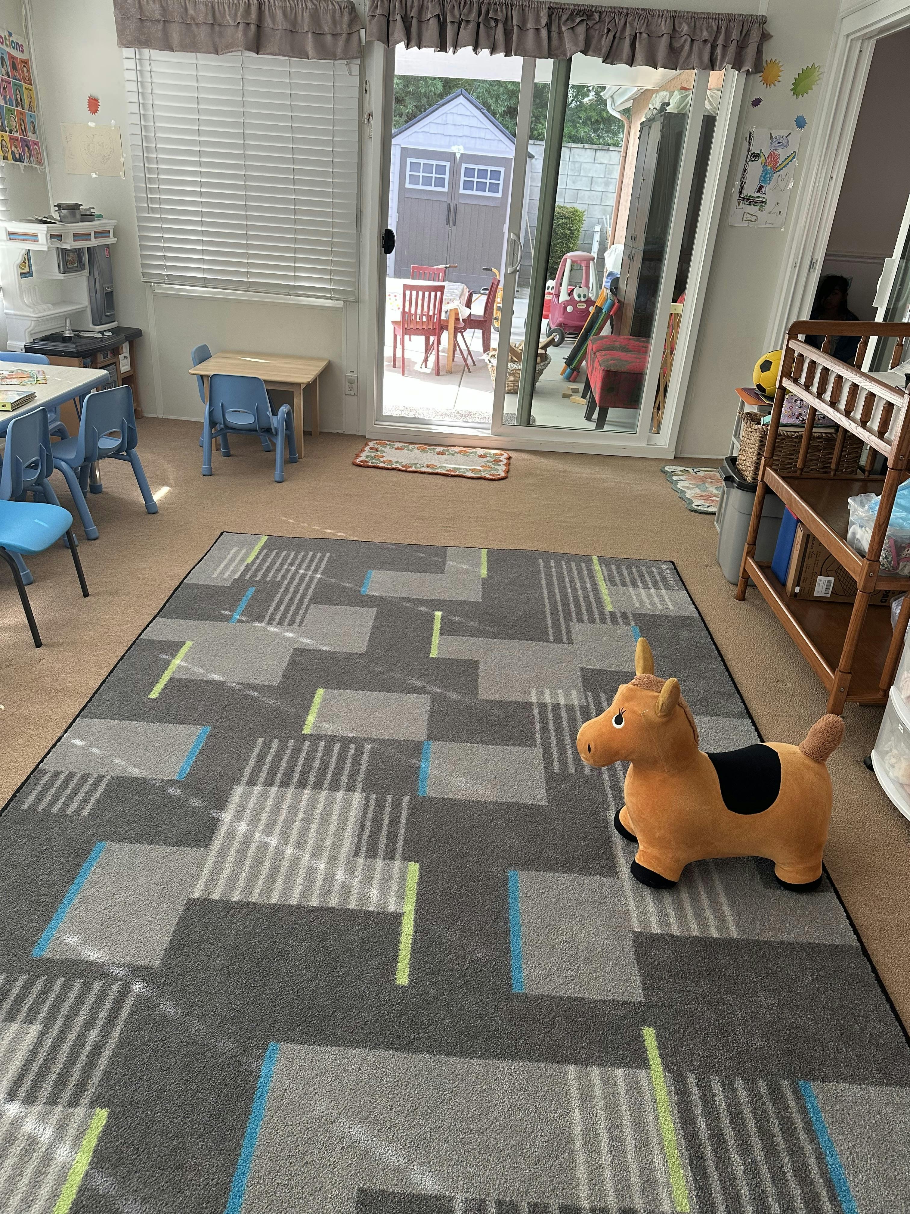 A playroom with small tables and chairs, a patterned rug, and a toy horse
