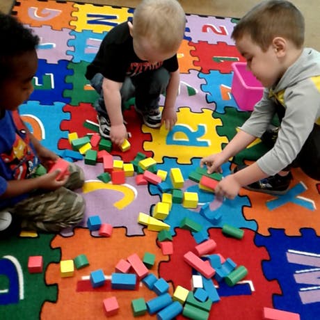 Three children playing with colorful blocks on a letter mat