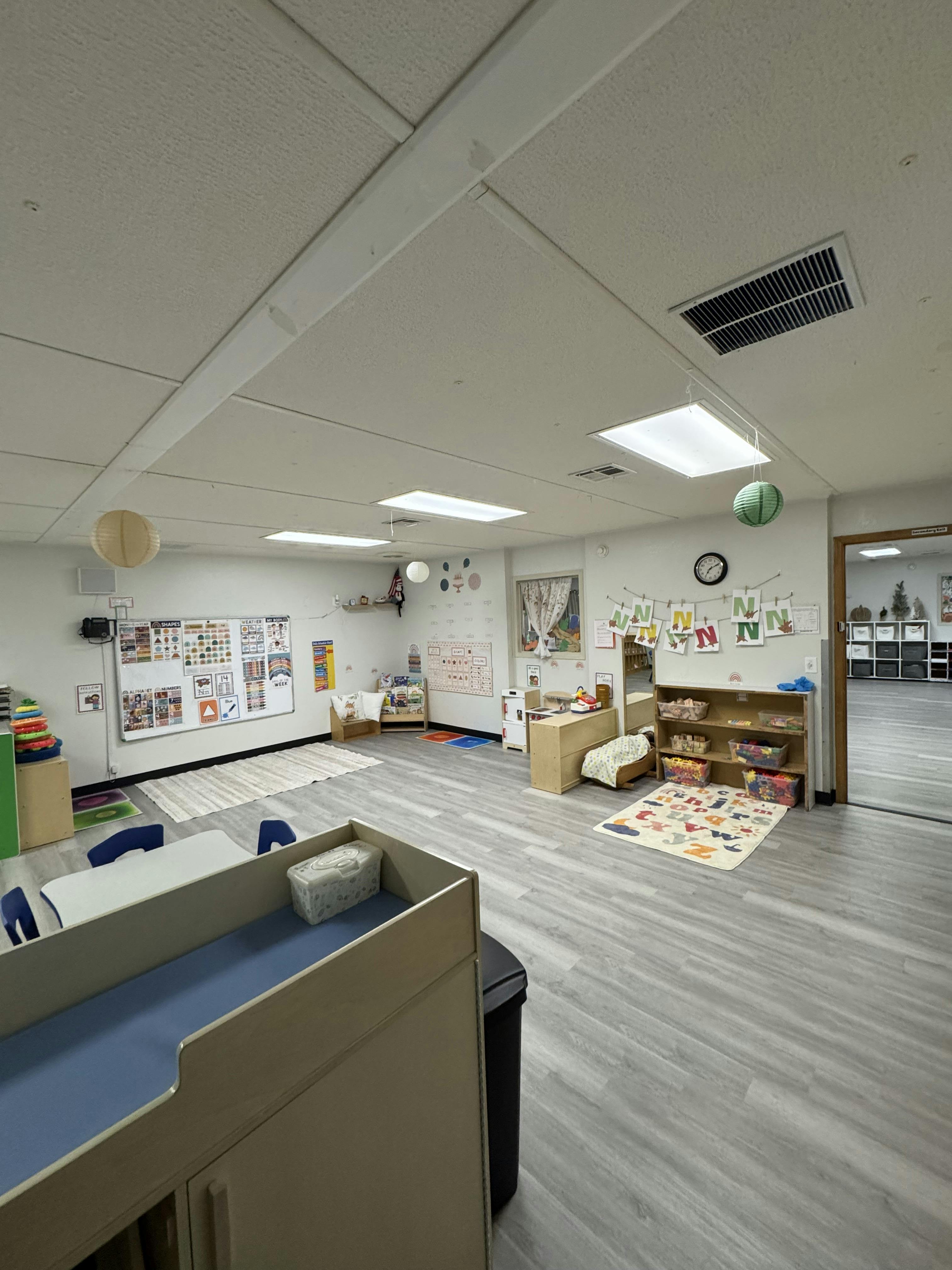 A brightly lit classroom with children's furniture, educational posters, and toys