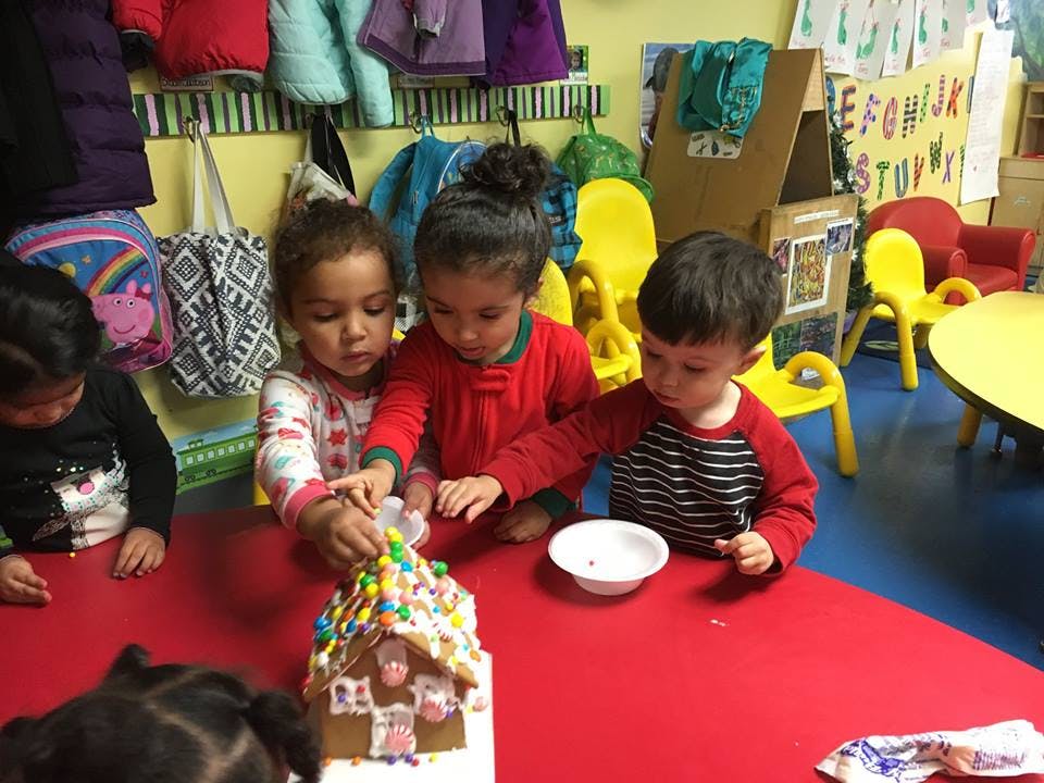 Children decorating a gingerbread house in a classroom