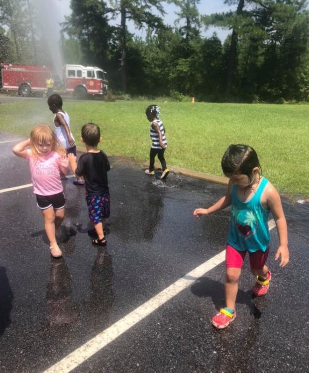Children playing in water from a fire truck hose on a paved surface