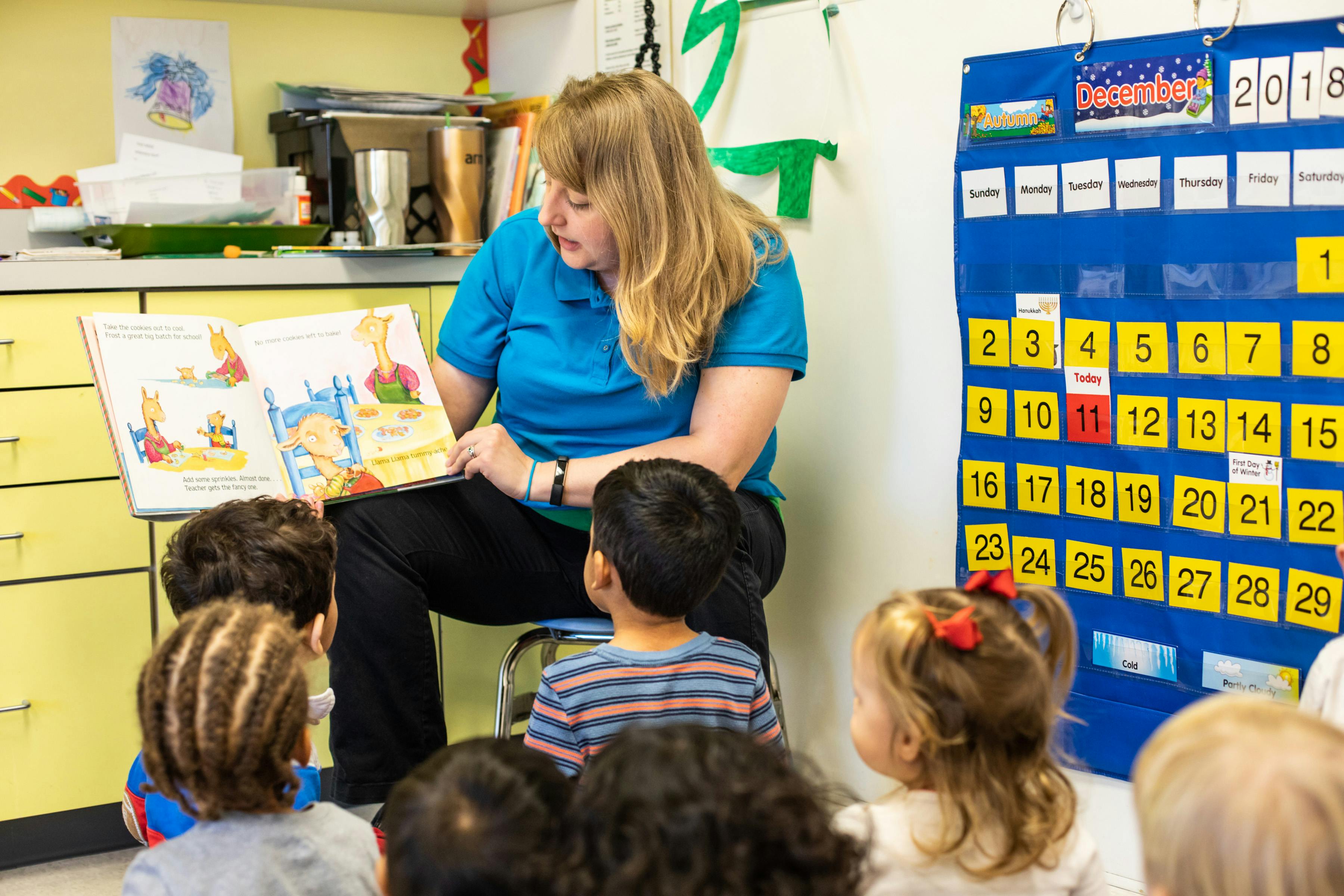 Person reading a book to a group of children in a classroom