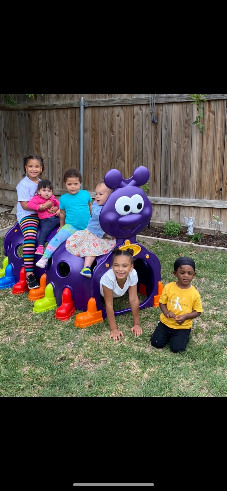 Children playing on a purple caterpillar-shaped play structure in a yard