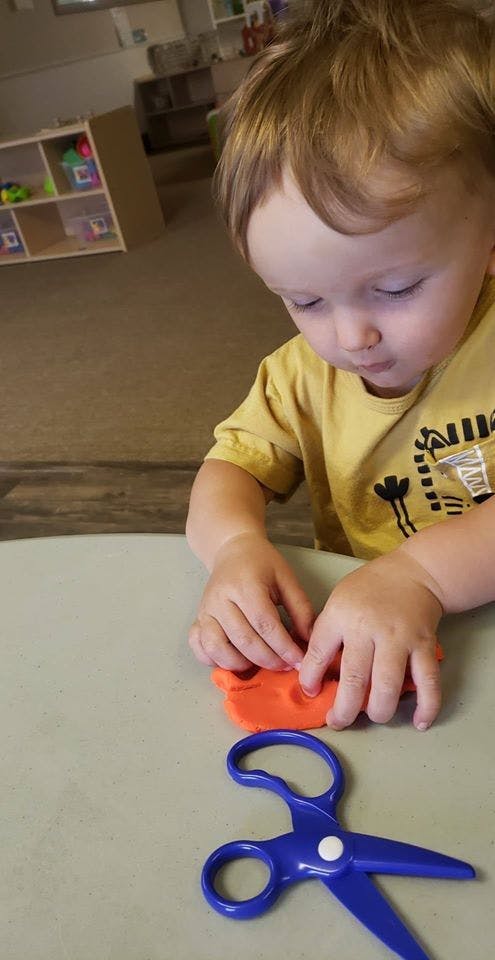 Child playing with orange modeling clay at a table