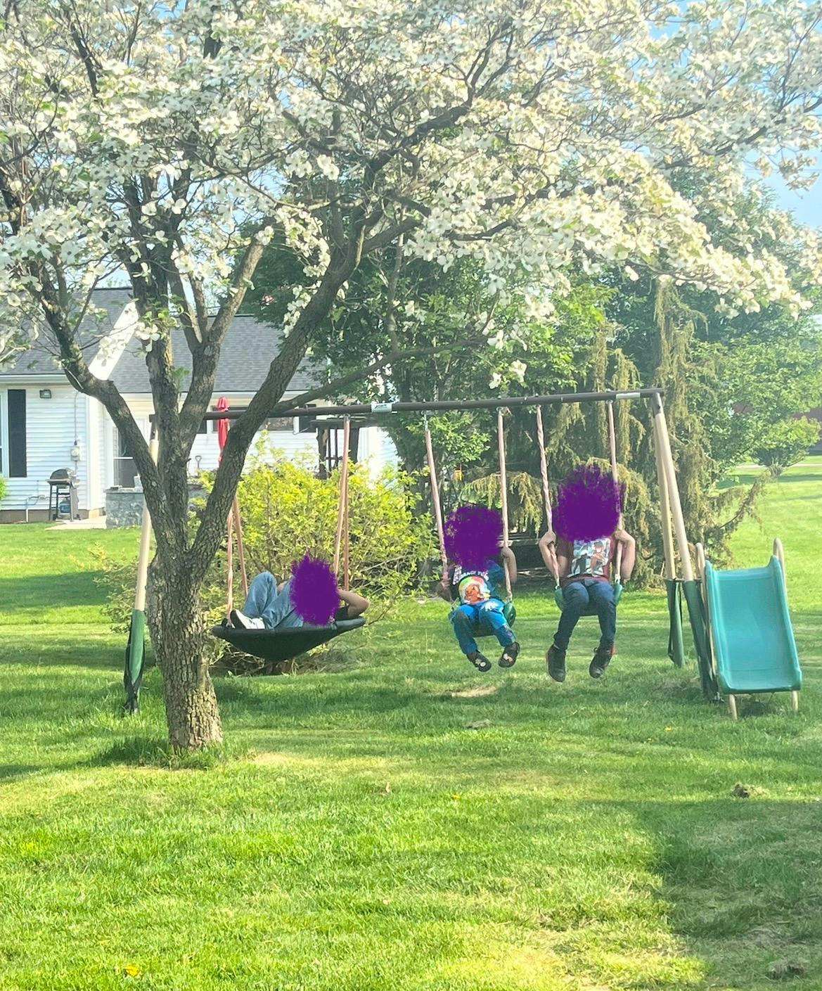 Three people on swings and a swing set in a grassy yard