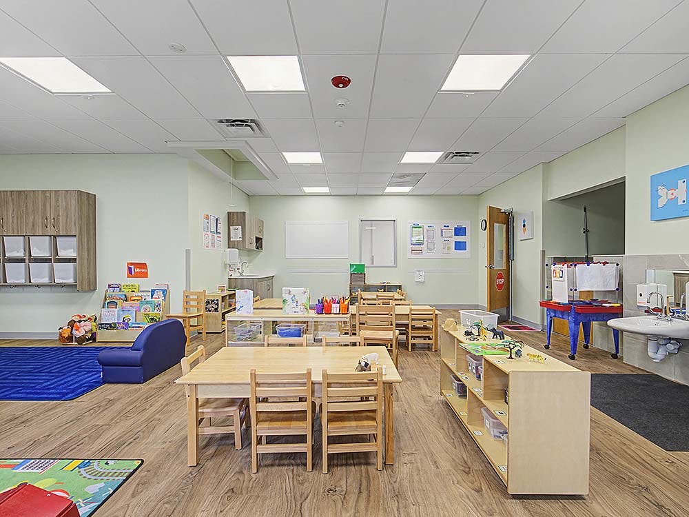 Empty classroom with small tables and chairs, and a play area