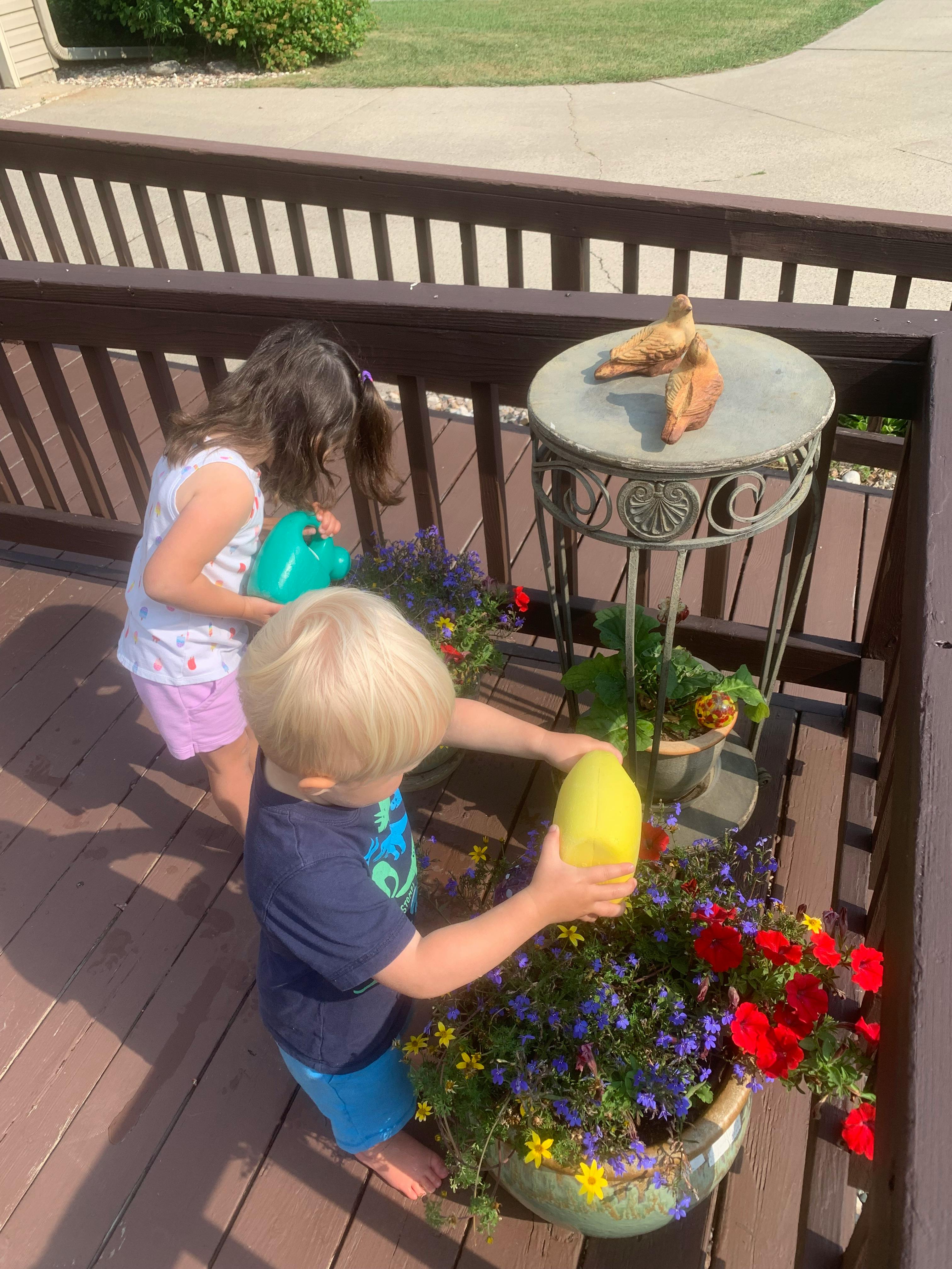 Two children watering plants on a deck