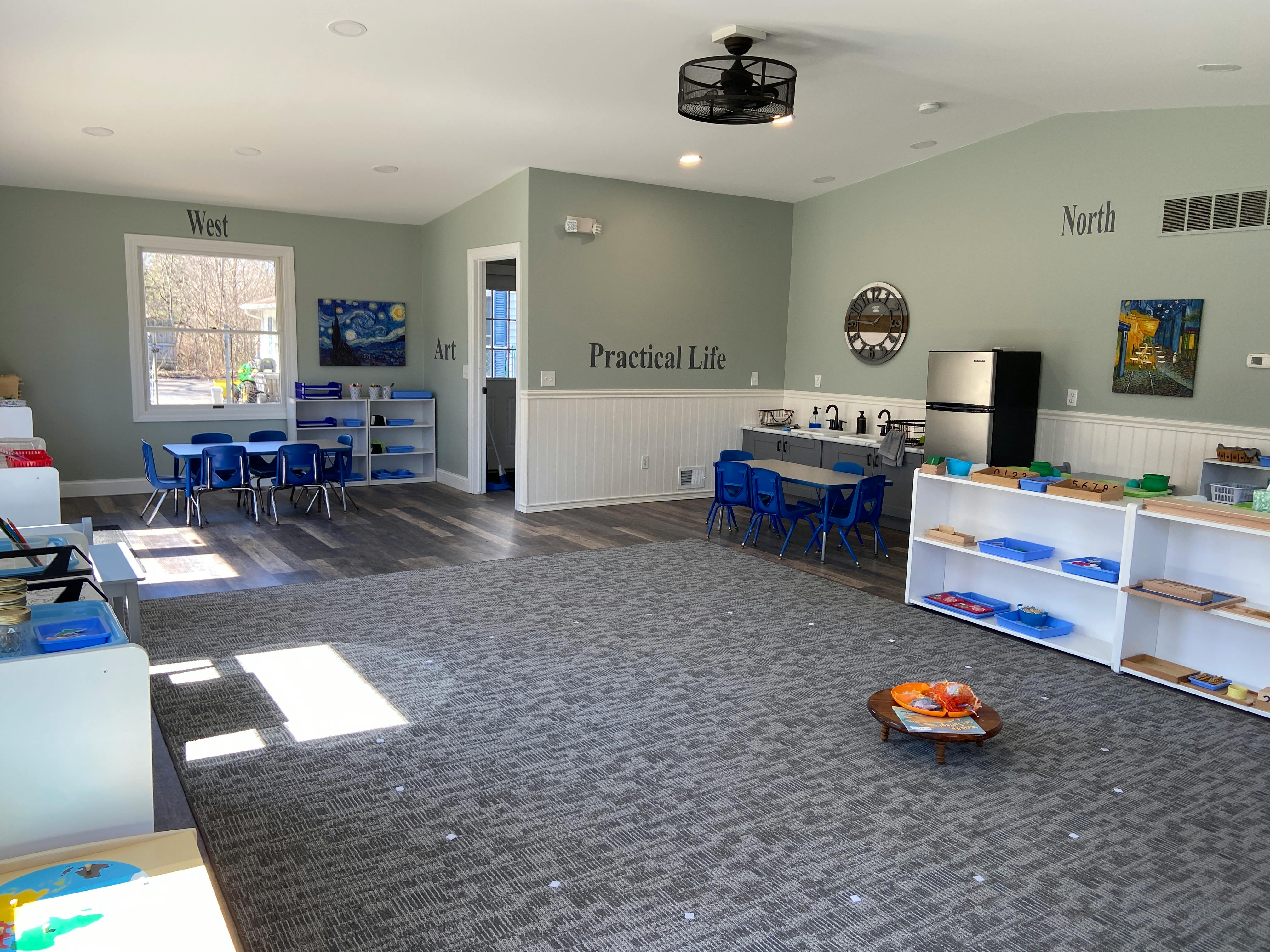 Empty classroom with small tables and chairs, shelves, and a refrigerator
