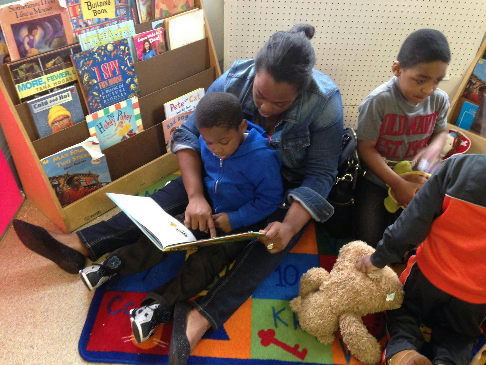 Adult and child reading a book together on the floor, other children nearby