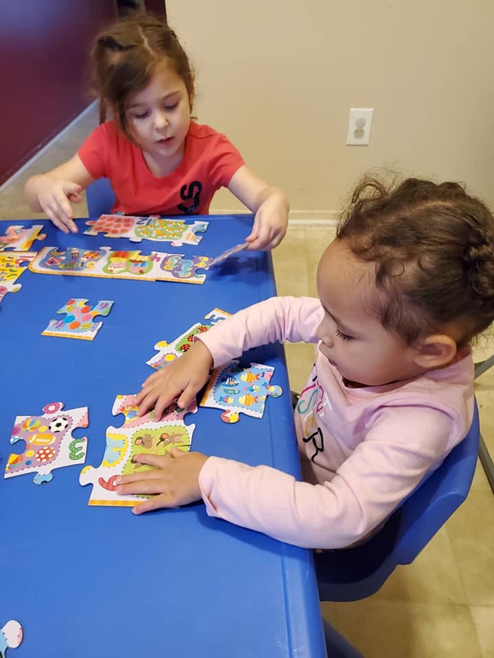 Two children playing with puzzles at a blue table
