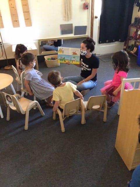 Adult wearing a mask reading a book to children in a classroom
