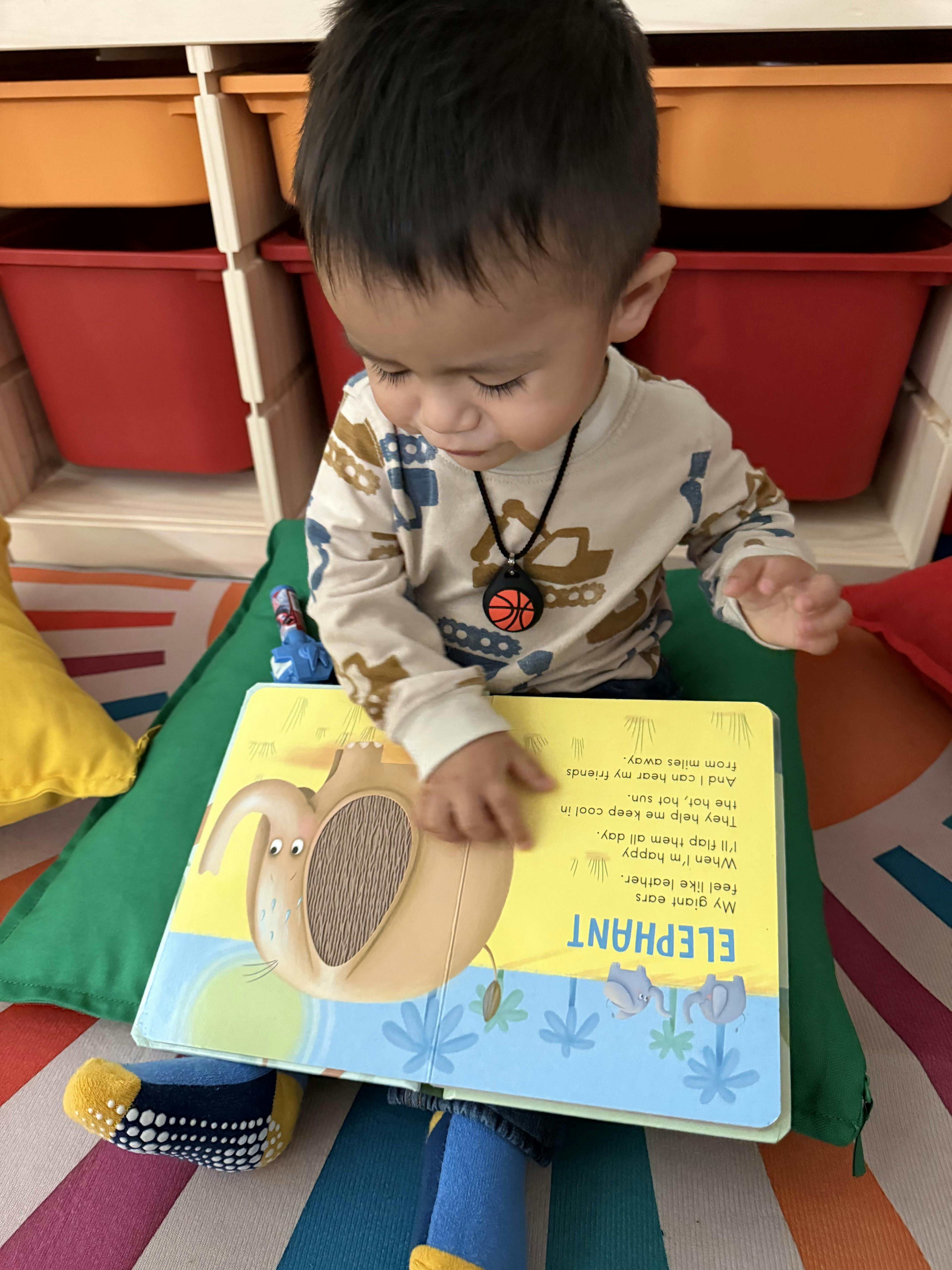 Child looking down at a book that says "ELEPHANT"