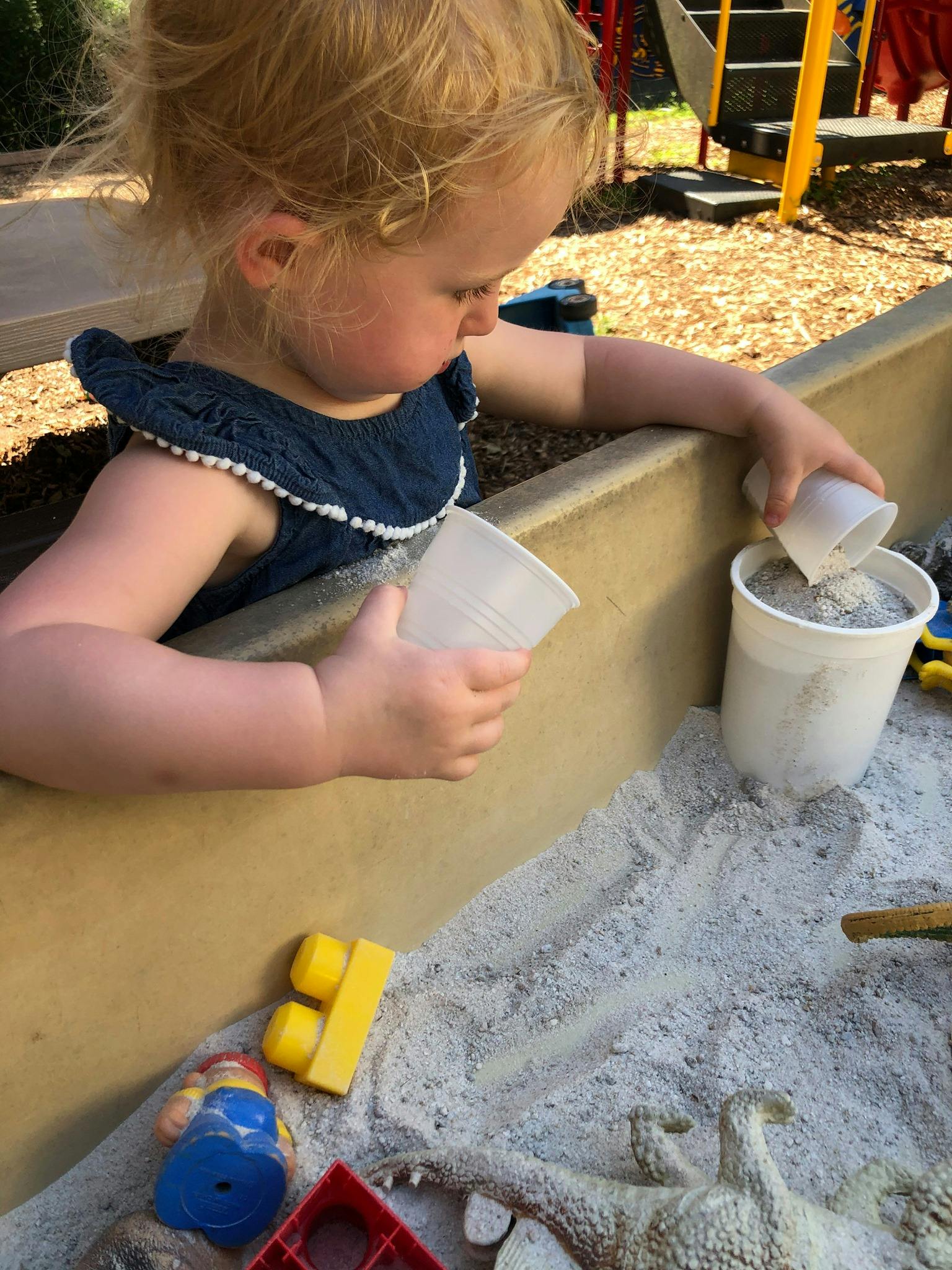 Child playing in a sandbox, pouring sand from one cup to another