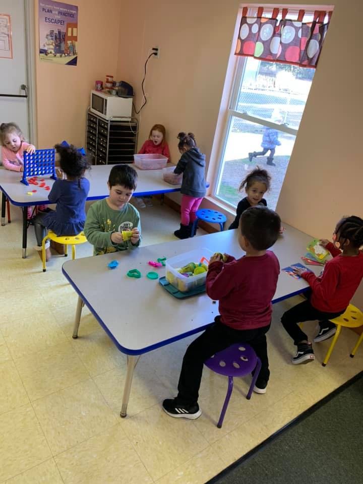 Children playing with toys and modeling clay at tables in a classroom