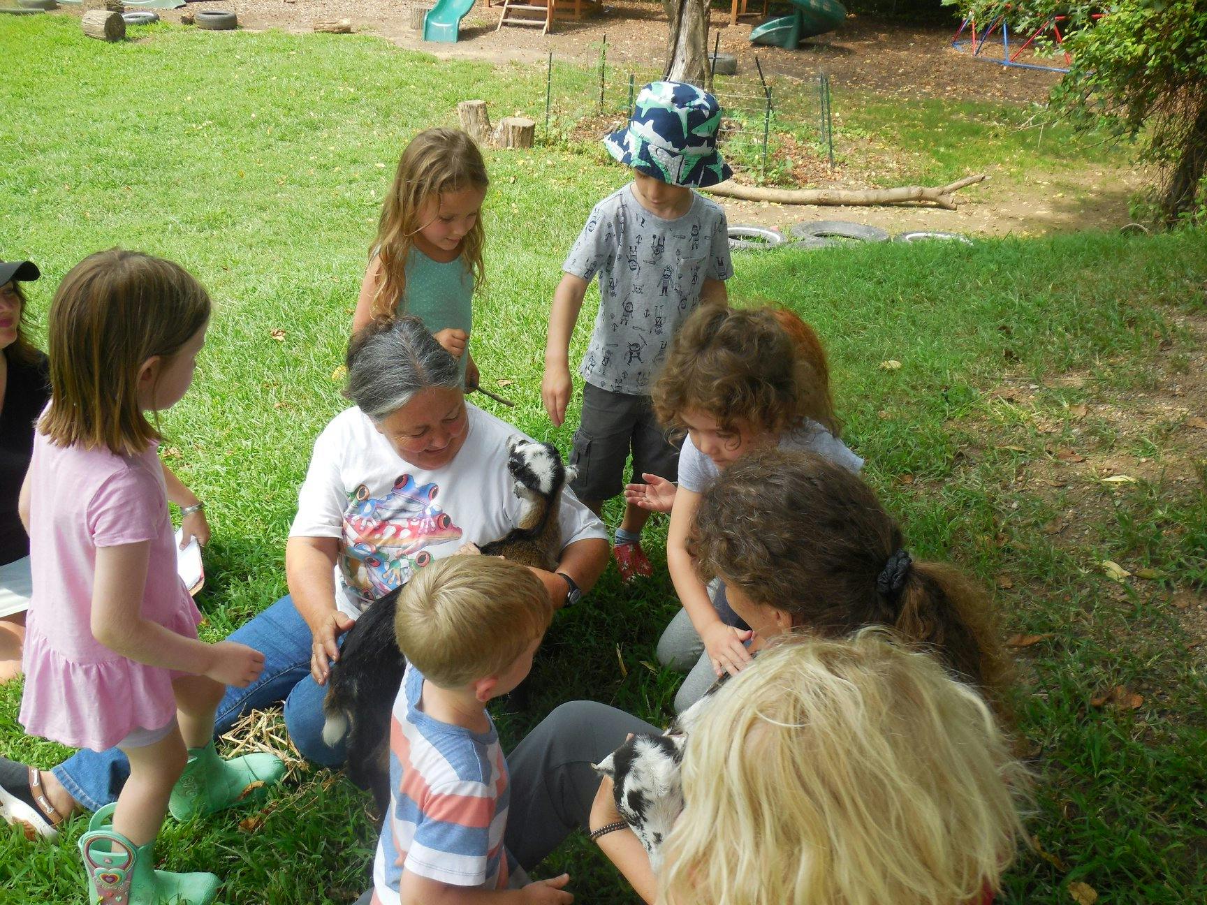 Adults and children gathered around small animals on grass