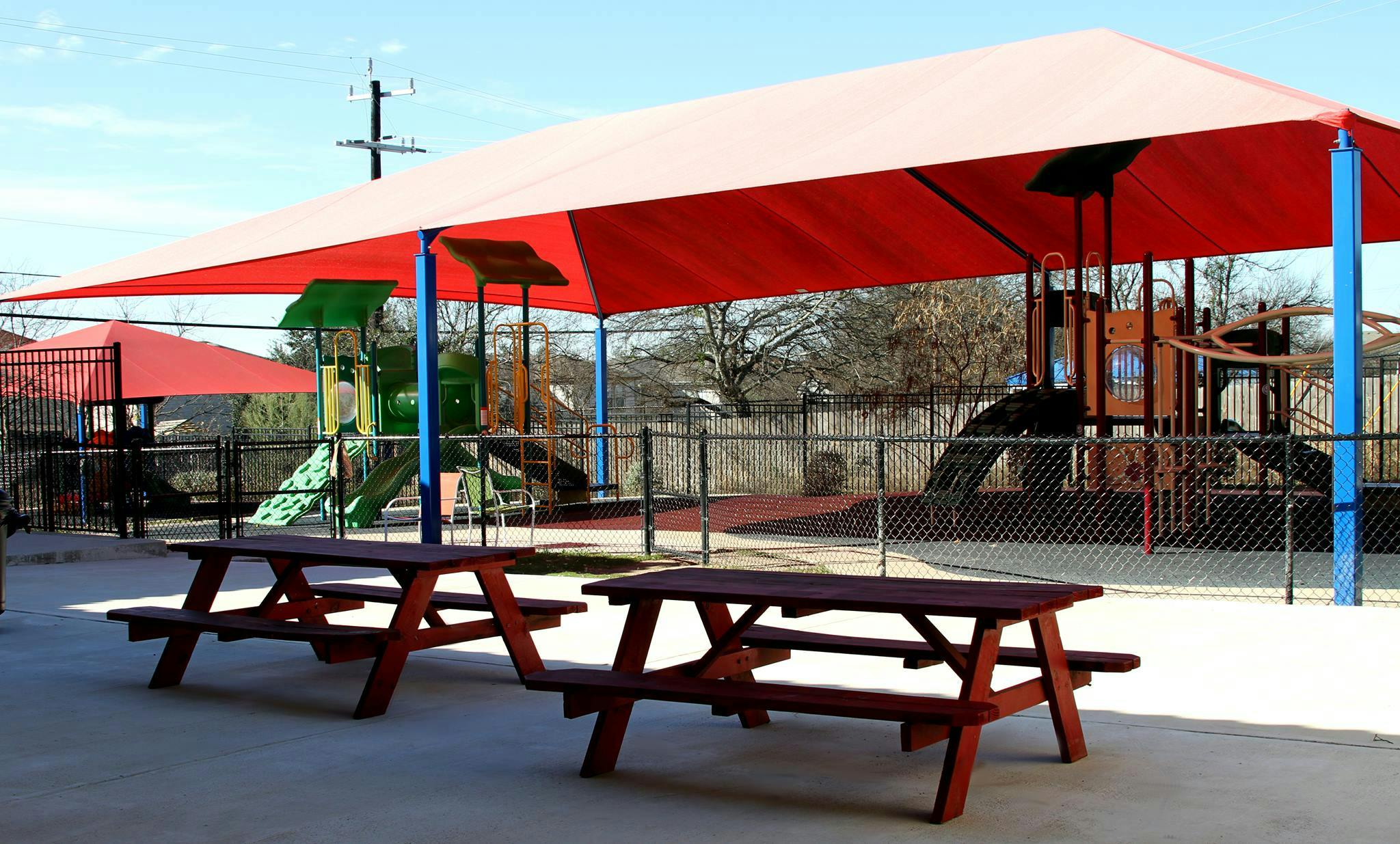 Picnic tables under a red shade structure at a playground