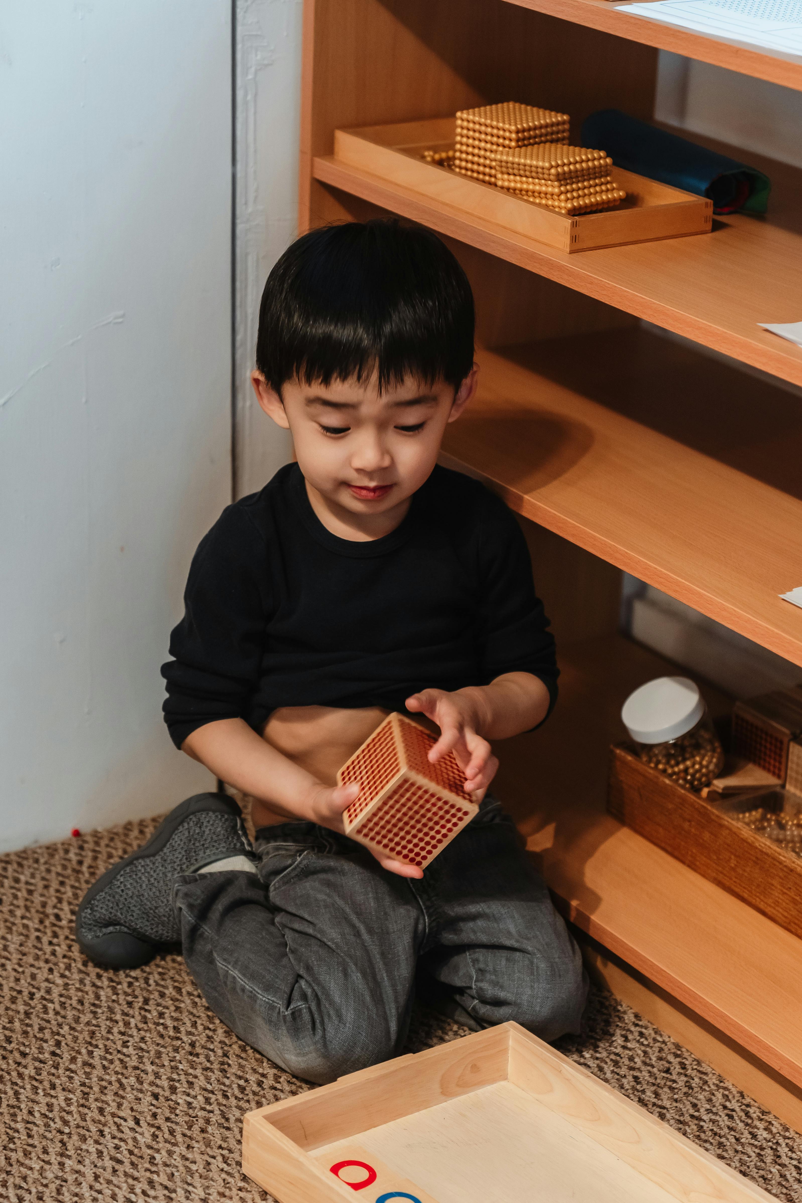 Child kneeling on floor holding a wooden cube