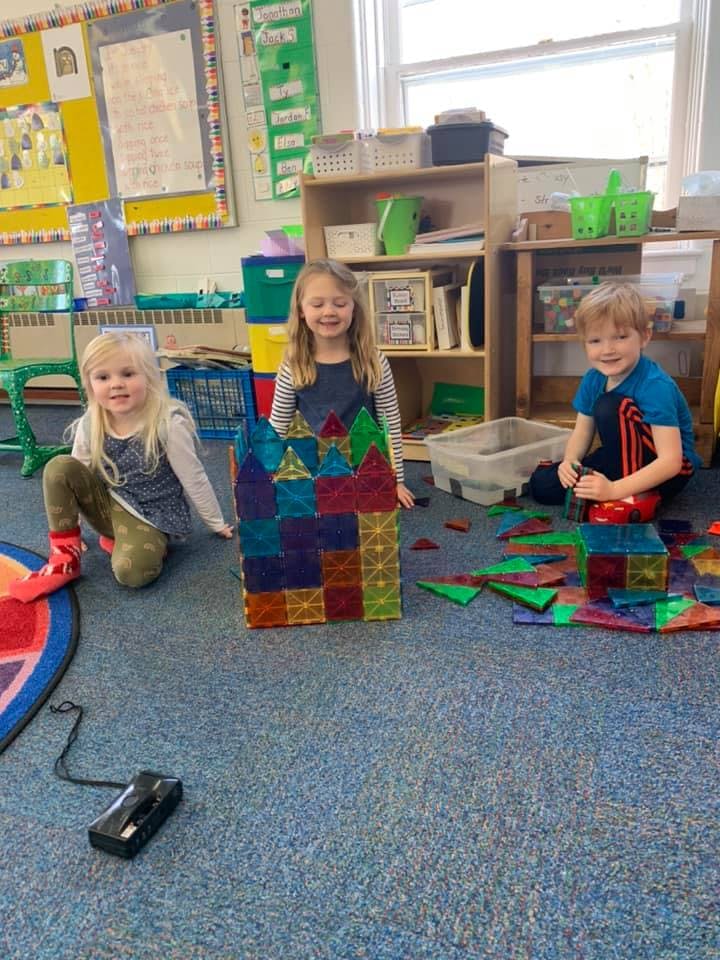 Three children playing with colorful magnetic tiles on the floor in a classroom