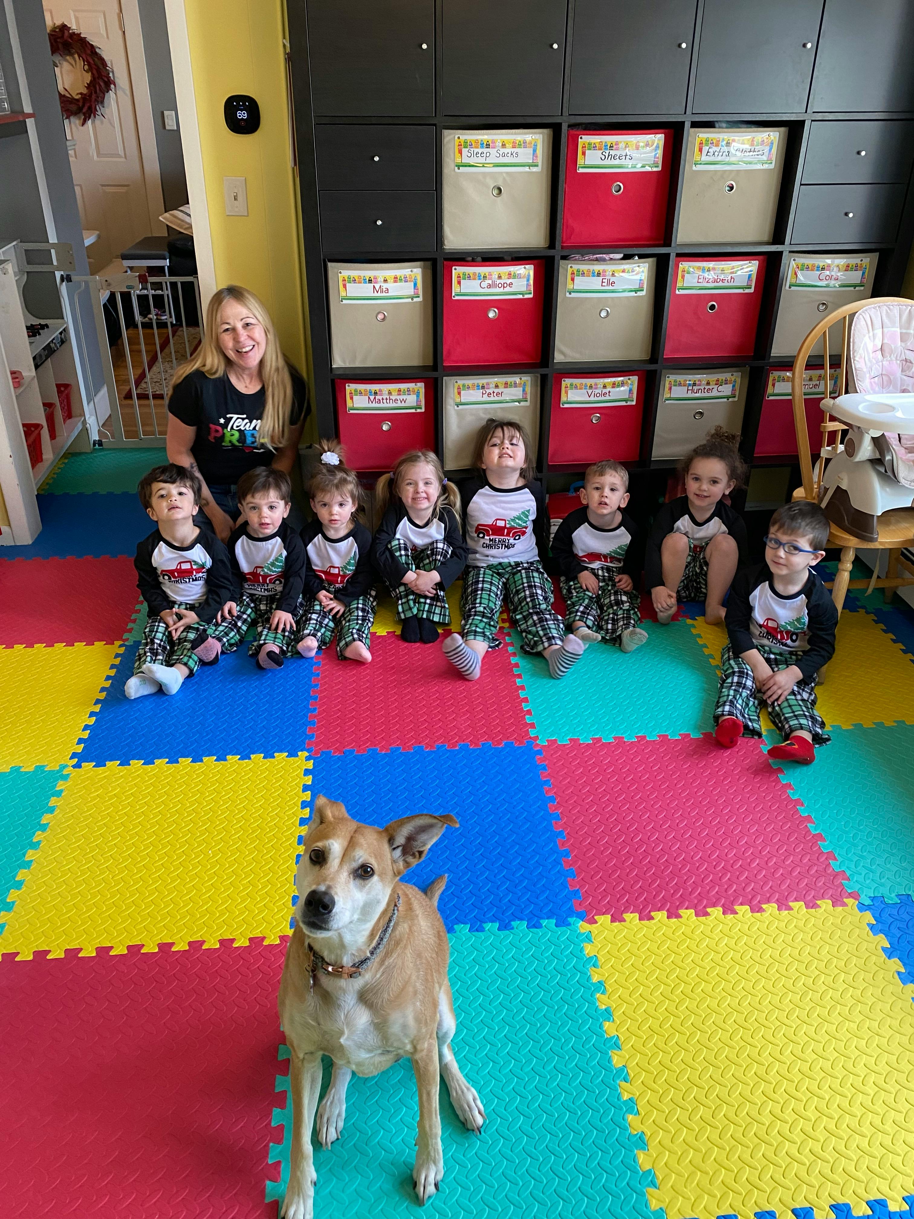 Adult and multiple children sitting on a colorful mat with a dog in the foreground