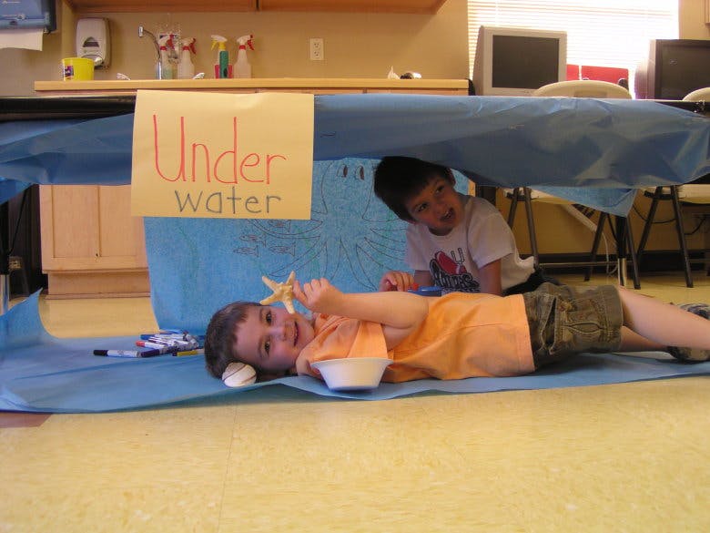 Two children playing under a table with a sign that says "Under Water"