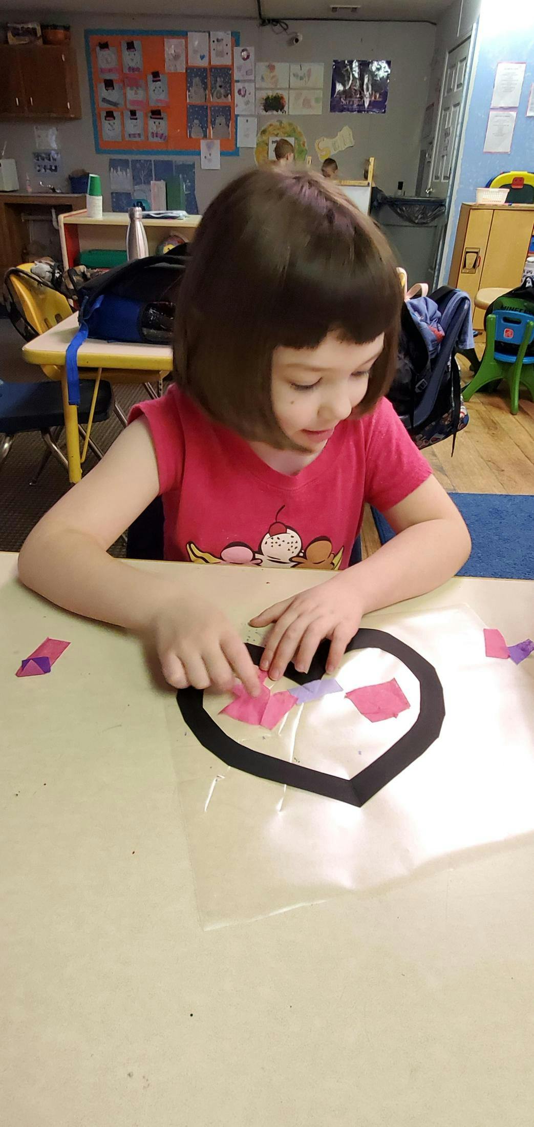 Child making a heart craft with colorful paper pieces