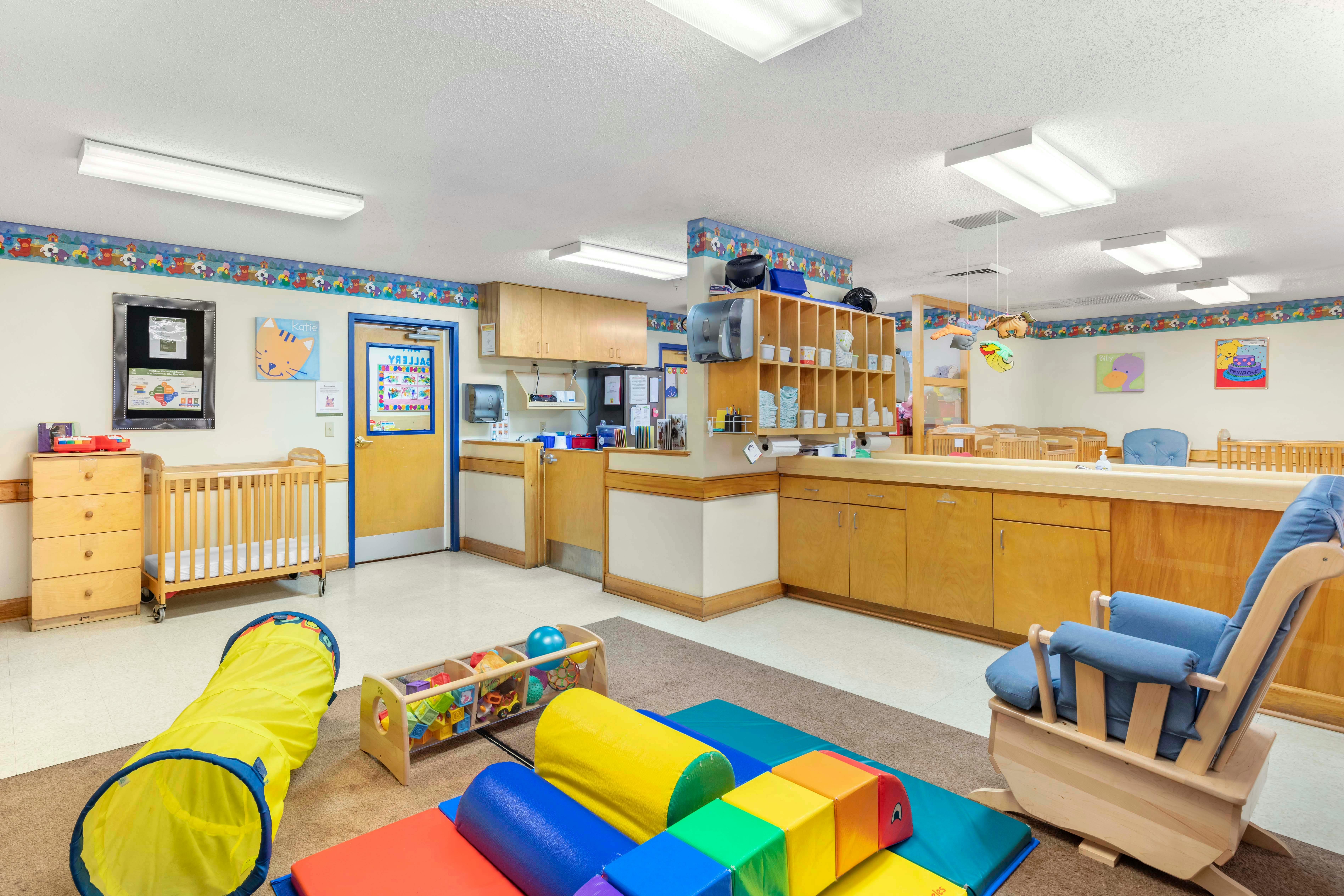 A colorful childcare room with cribs, play equipment, and changing stations