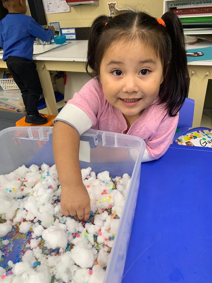 Child playing with cotton balls and colorful beads in a clear bin